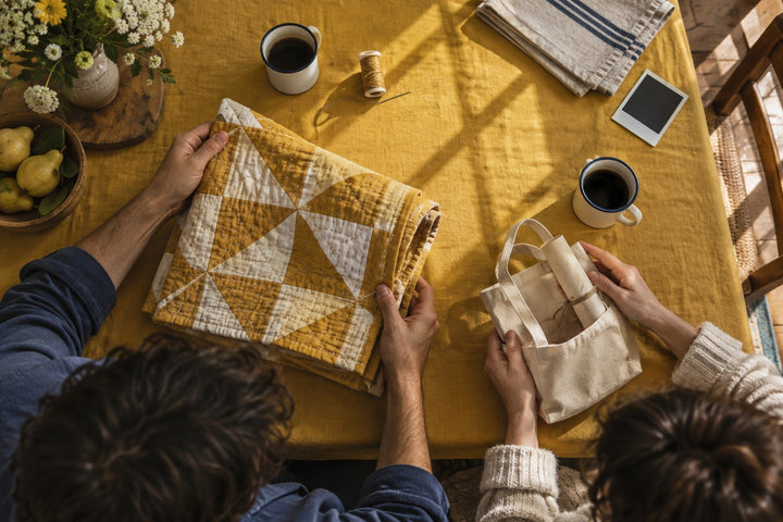 Noces de coton : vue de dessus d'un couple échangeant un carré de coton cousu et une pochette en tissu sur une nappe moutarde
