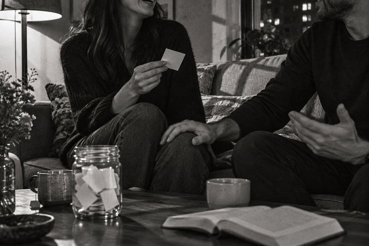Questions pour couple : en noir et blanc, un couple sur un canapé, une carte de question à la main et un bocal de papiers pliés